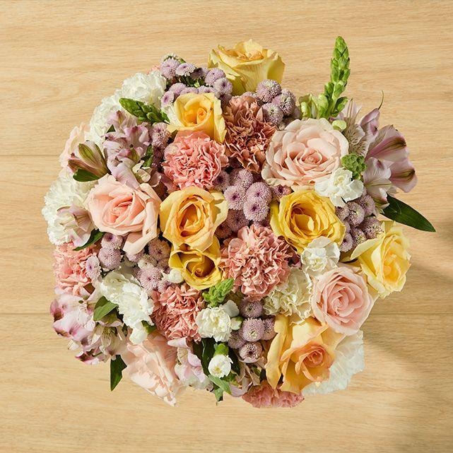 Peach and yellow roses, carnations, alstroemeria, lavender poms, and white snapdragons.
