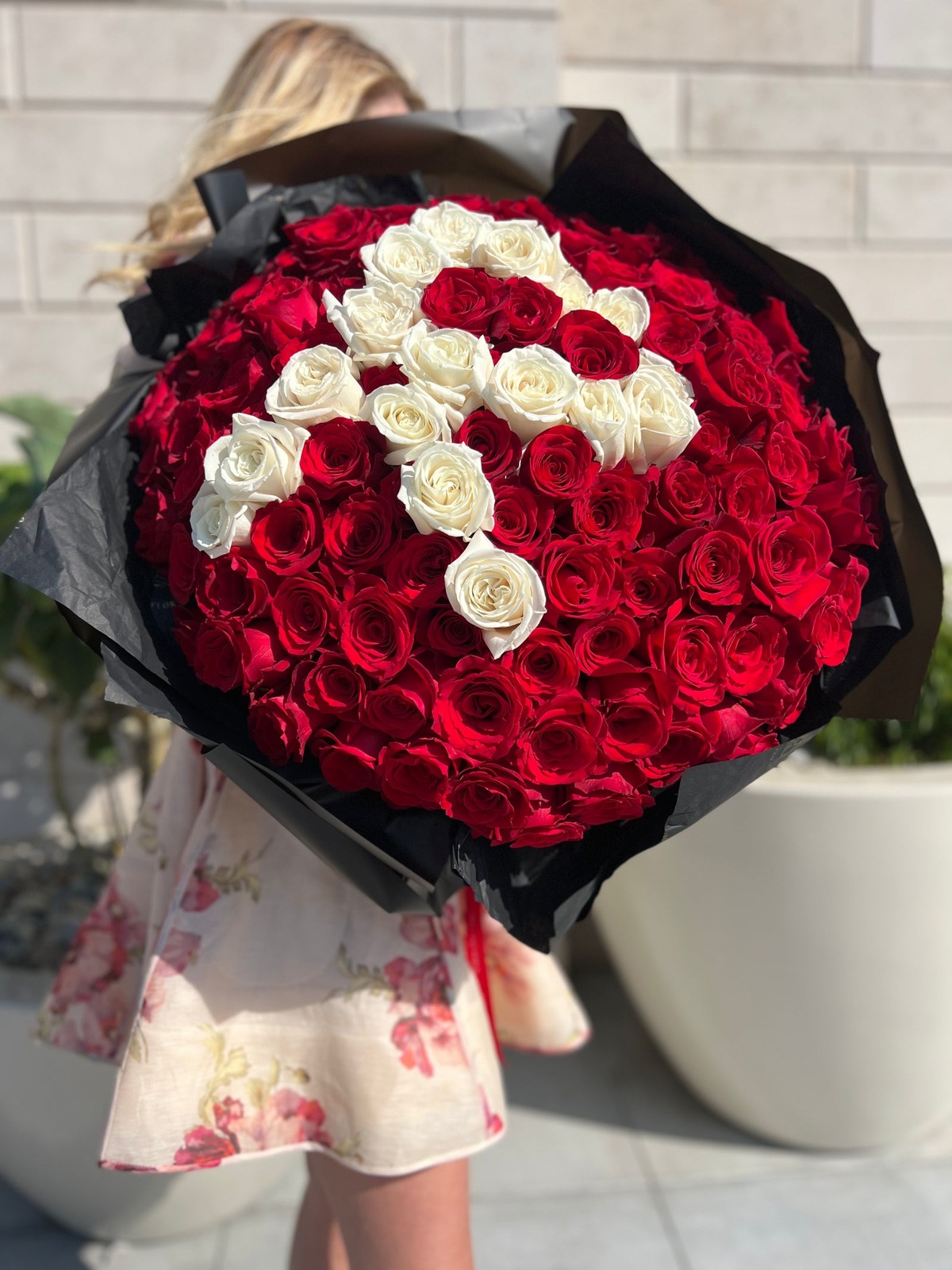 A large bouquet of red and white roses in black wrapping.